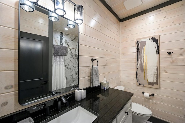 bathroom featuring vanity, toilet, and wooden walls