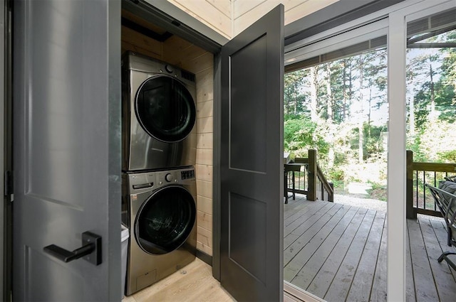 clothes washing area featuring stacked washer / drying machine, wooden walls, and light hardwood / wood-style flooring