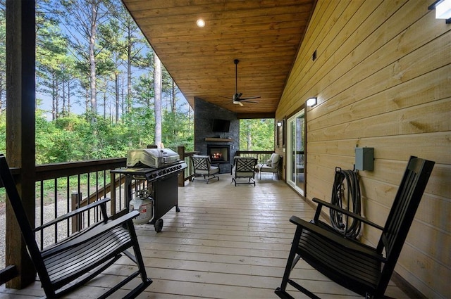 wooden deck featuring an outdoor stone fireplace, ceiling fan, and grilling area