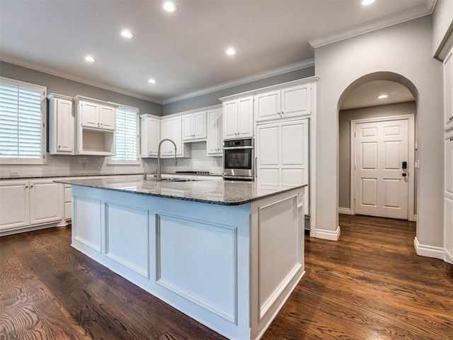 kitchen with dark wood-type flooring, appliances with stainless steel finishes, and an island with sink