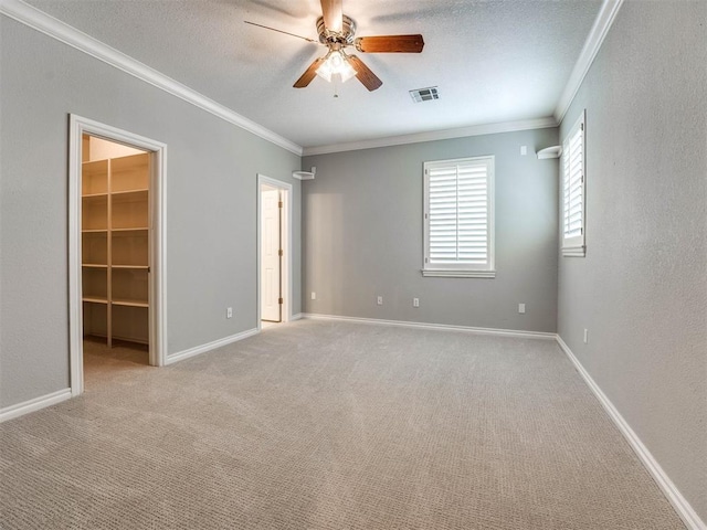 unfurnished bedroom featuring light carpet, a walk in closet, ceiling fan, and ornamental molding