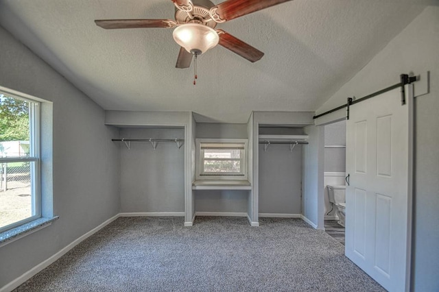 unfurnished bedroom featuring carpet, a textured ceiling, a barn door, and ceiling fan