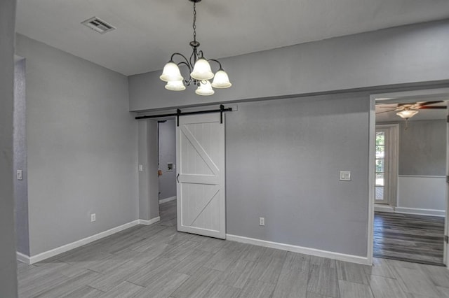 spare room featuring light wood-type flooring, a barn door, and ceiling fan with notable chandelier