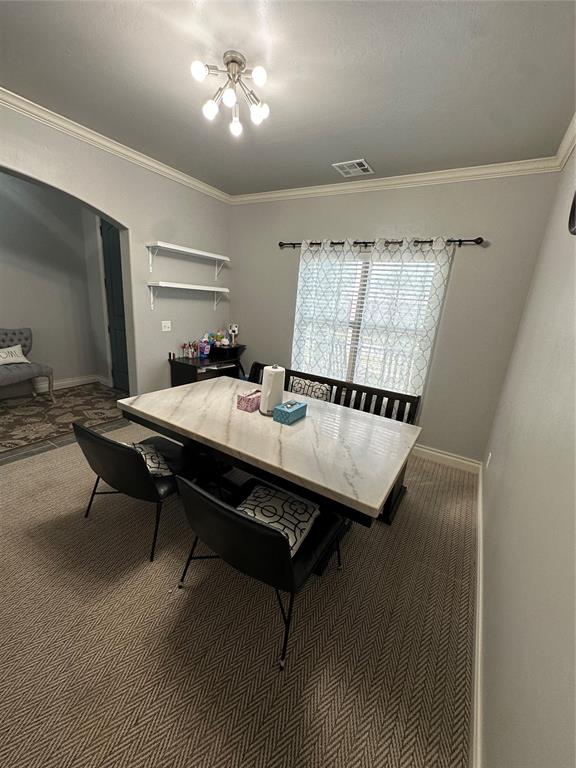 dining area featuring an inviting chandelier, dark carpet, and crown molding