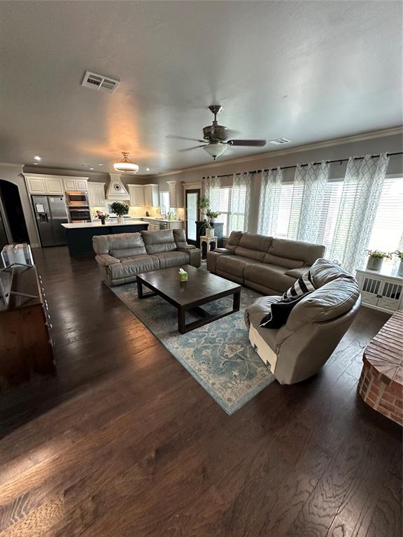 living room with crown molding, ceiling fan, and dark wood-type flooring