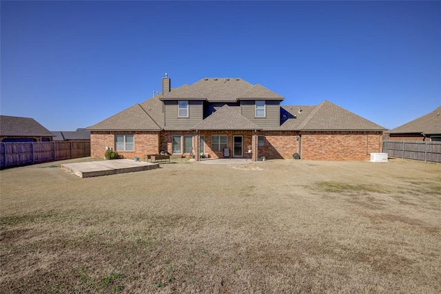 rear view of house featuring brick siding, a chimney, a fenced backyard, and a lawn