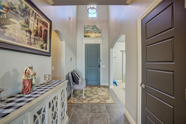 entrance foyer featuring arched walkways, dark tile patterned flooring, a high ceiling, and baseboards