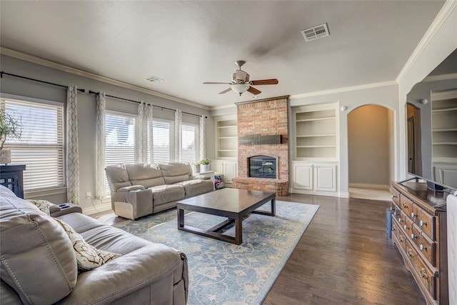 living room with arched walkways, built in features, visible vents, crown molding, and a fireplace