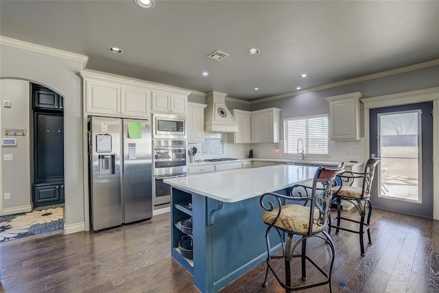 kitchen with arched walkways, a center island, custom exhaust hood, visible vents, and appliances with stainless steel finishes