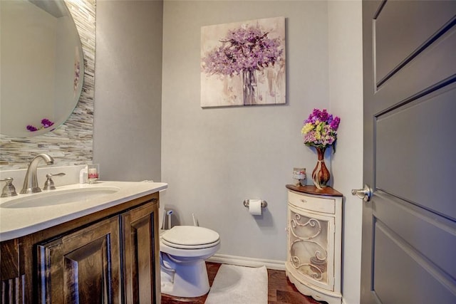 half bath with toilet, baseboards, and vanity