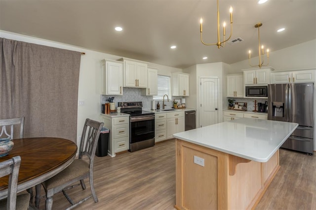 kitchen with white cabinets, hanging light fixtures, vaulted ceiling, appliances with stainless steel finishes, and a kitchen island