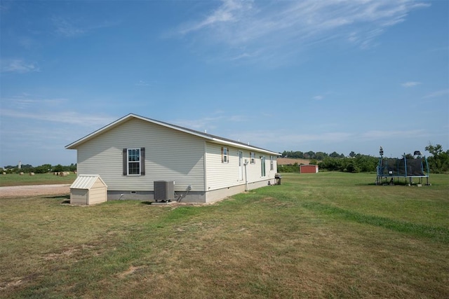 view of side of property featuring cooling unit, a trampoline, and a yard