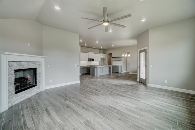 unfurnished living room featuring ceiling fan with notable chandelier, vaulted ceiling, light hardwood / wood-style flooring, and a stone fireplace