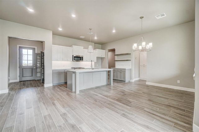 kitchen with decorative light fixtures, light hardwood / wood-style flooring, and a kitchen island with sink