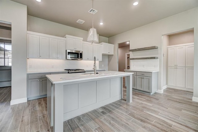 kitchen featuring appliances with stainless steel finishes, a center island with sink, light hardwood / wood-style flooring, and sink