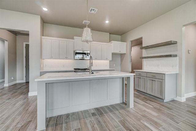 kitchen with backsplash, a kitchen island with sink, sink, and light wood-type flooring