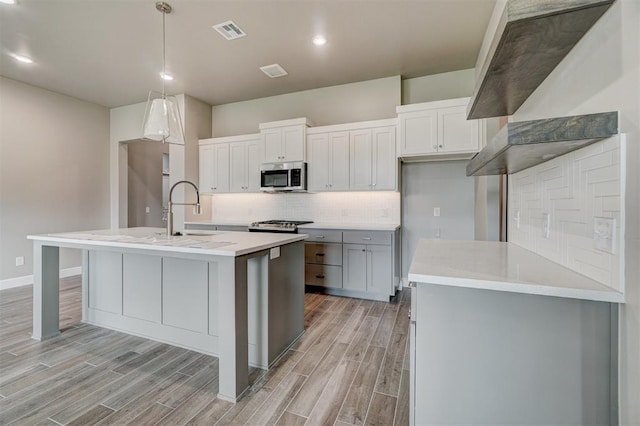 kitchen with pendant lighting, sink, light hardwood / wood-style flooring, an island with sink, and stainless steel appliances