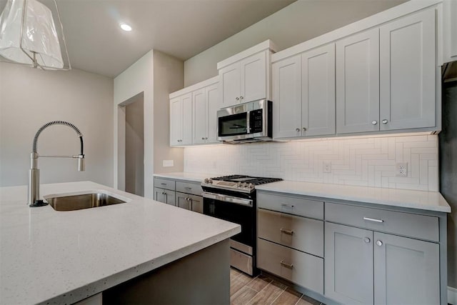 kitchen with pendant lighting, backsplash, sink, light wood-type flooring, and appliances with stainless steel finishes