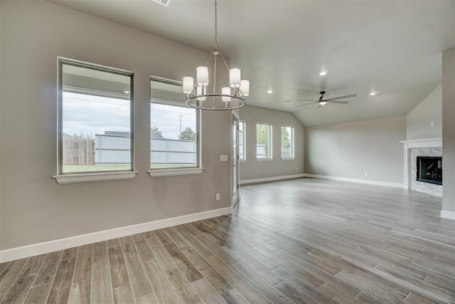 unfurnished living room with ceiling fan with notable chandelier, light wood-type flooring, vaulted ceiling, and a premium fireplace