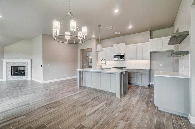 kitchen featuring pendant lighting, white cabinets, light hardwood / wood-style flooring, an island with sink, and a notable chandelier