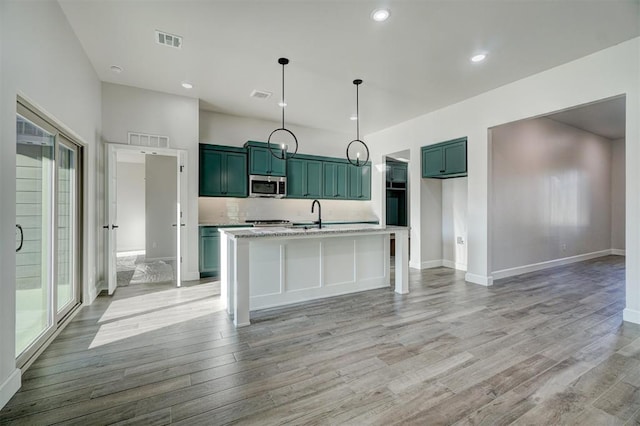 kitchen featuring sink, light stone counters, light hardwood / wood-style flooring, an island with sink, and decorative light fixtures