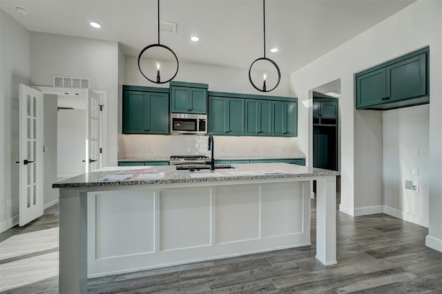 kitchen featuring light stone countertops, pendant lighting, light hardwood / wood-style flooring, and an island with sink