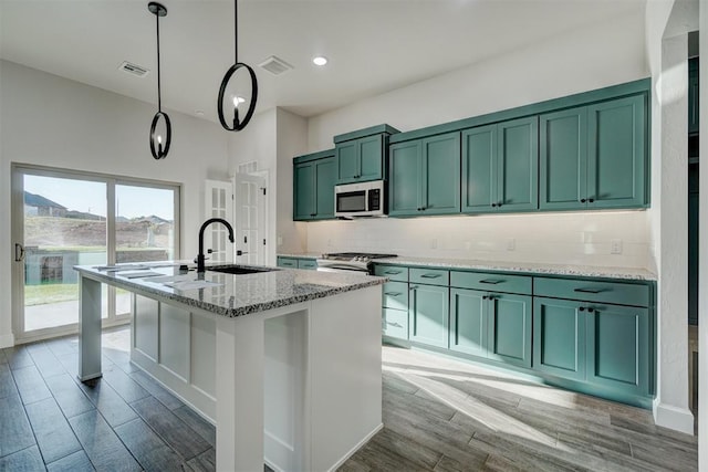 kitchen featuring light stone countertops, appliances with stainless steel finishes, a center island with sink, hardwood / wood-style flooring, and green cabinets