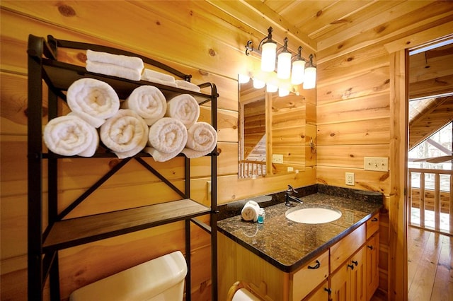 bathroom featuring toilet, wooden walls, vanity, wood ceiling, and hardwood / wood-style flooring