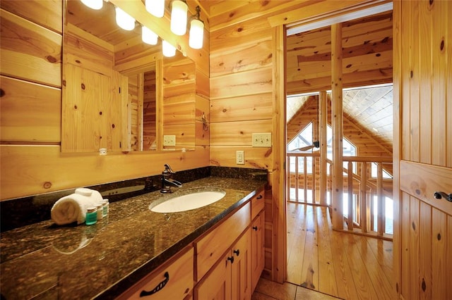 bathroom with hardwood / wood-style floors, vanity, wood walls, and vaulted ceiling