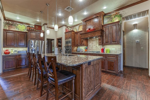 kitchen with appliances with stainless steel finishes, ornamental molding, a textured ceiling, pendant lighting, and an island with sink