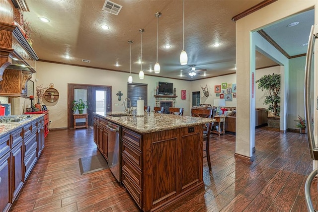 kitchen featuring light stone counters, a textured ceiling, sink, pendant lighting, and an island with sink