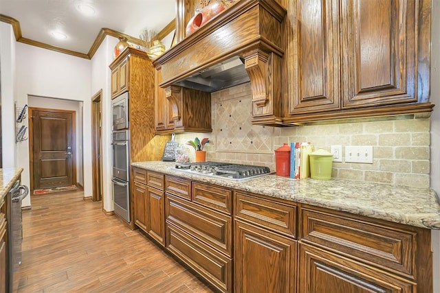 kitchen with light stone counters, light hardwood / wood-style flooring, crown molding, decorative backsplash, and appliances with stainless steel finishes