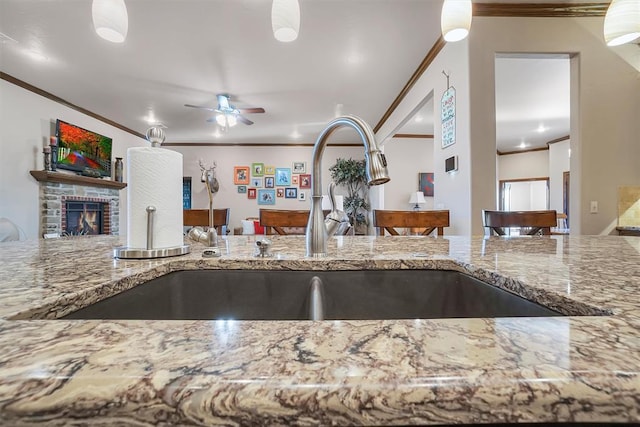11335 N 1930th Rd, Sayre, OK 73662 - kitchen with crown molding, light stone counters, a ceiling fan, a fireplace, and a sink