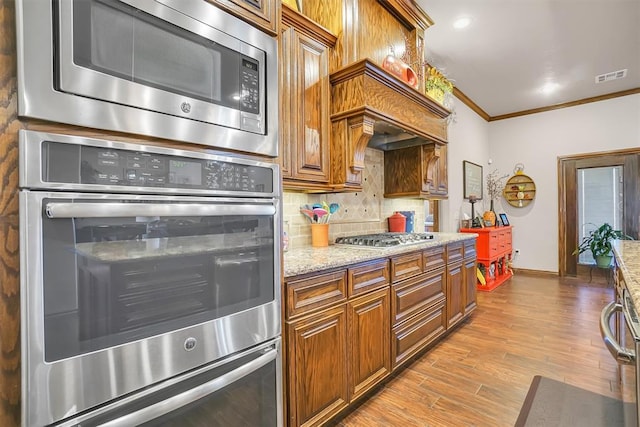 kitchen featuring light hardwood / wood-style floors, light stone counters, crown molding, and appliances with stainless steel finishes