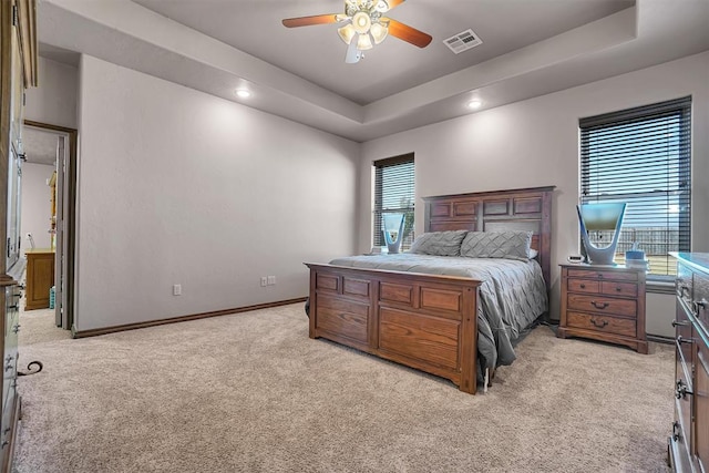 bedroom with light colored carpet, a raised ceiling, and ceiling fan