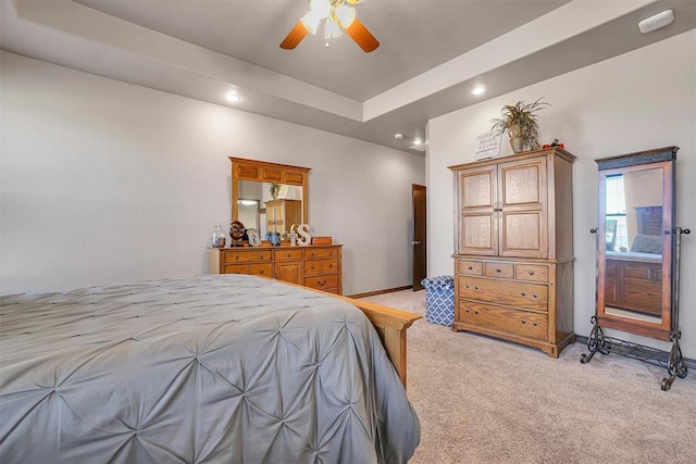 carpeted bedroom with a raised ceiling, ensuite bath, and ceiling fan