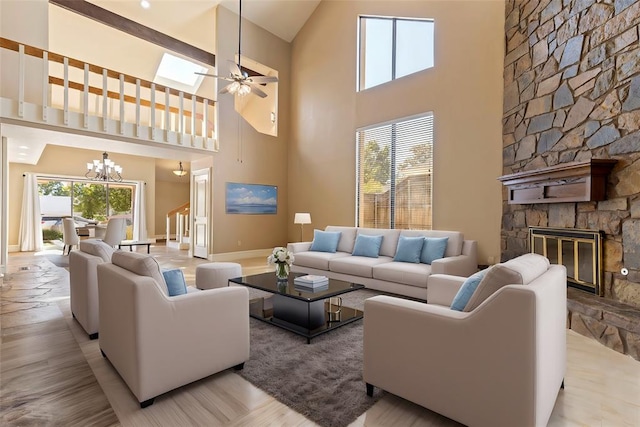 living room featuring a stone fireplace, a skylight, ceiling fan with notable chandelier, and a high ceiling