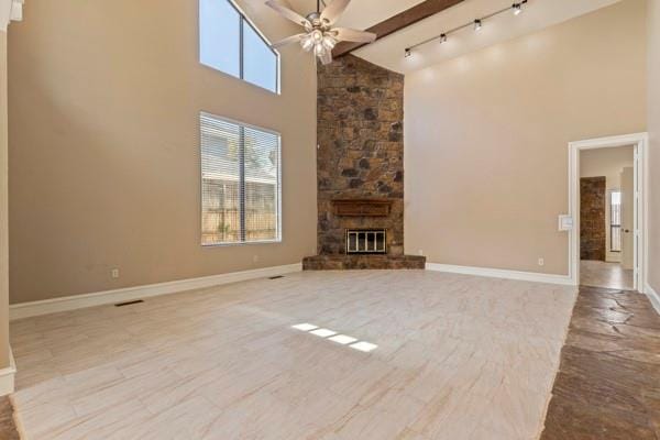 unfurnished living room featuring beam ceiling, a stone fireplace, high vaulted ceiling, and ceiling fan