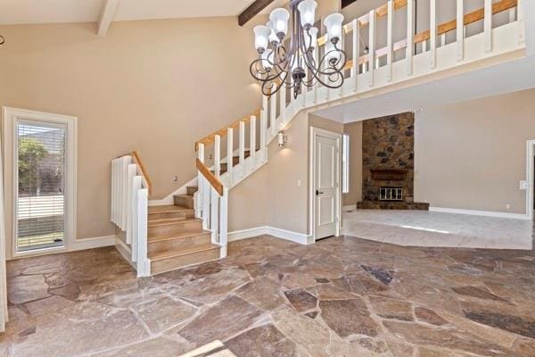 entrance foyer with beam ceiling, a stone fireplace, an inviting chandelier, and high vaulted ceiling