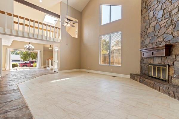 unfurnished living room with a stone fireplace, a towering ceiling, ceiling fan with notable chandelier, and a skylight