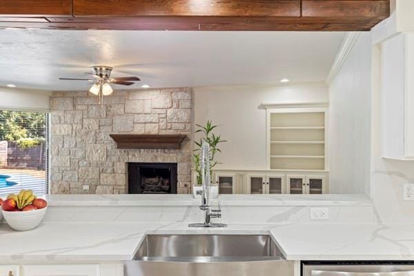 kitchen with sink, ceiling fan, light stone counters, a fireplace, and stainless steel dishwasher