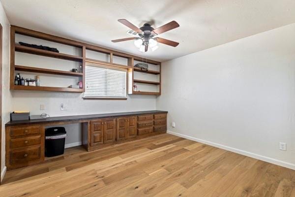 unfurnished office with ceiling fan, built in desk, and light hardwood / wood-style flooring