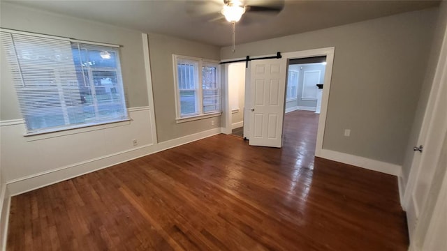 unfurnished bedroom featuring a barn door, ceiling fan, and dark hardwood / wood-style floors