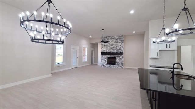 kitchen featuring white cabinets, light hardwood / wood-style floors, a stone fireplace, and hanging light fixtures