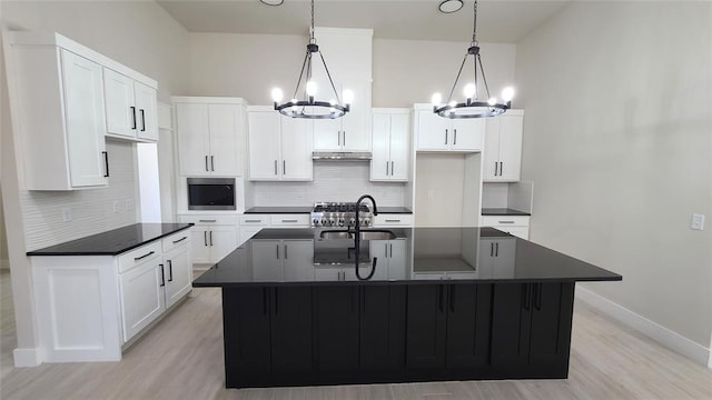 kitchen featuring tasteful backsplash, a kitchen island with sink, sink, decorative light fixtures, and a notable chandelier