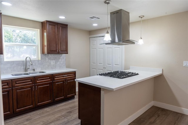 kitchen featuring sink, tasteful backsplash, pendant lighting, island range hood, and light wood-type flooring