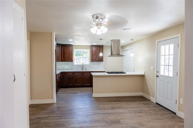 kitchen featuring kitchen peninsula, tasteful backsplash, sink, wall chimney range hood, and wood-type flooring