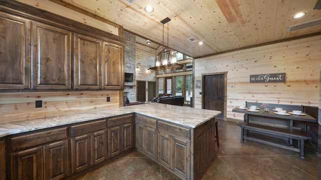 kitchen featuring kitchen peninsula, light stone counters, dark tile patterned floors, wooden walls, and decorative light fixtures