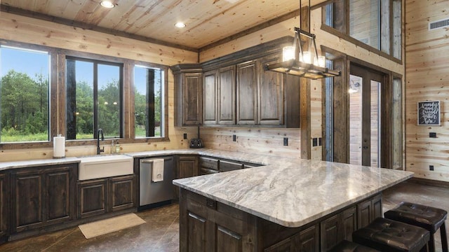 kitchen featuring dark brown cabinetry, wooden walls, sink, decorative light fixtures, and dishwasher