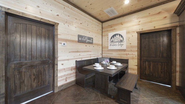 dining room featuring breakfast area, dark tile patterned flooring, wood ceiling, and wood walls